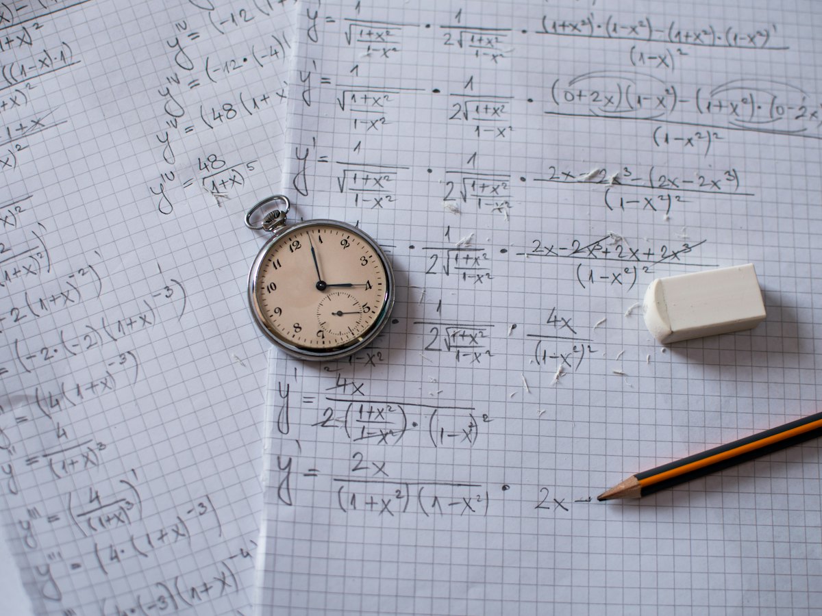A pocket watch, an eraser and a pencil on pages of handwritten maths.