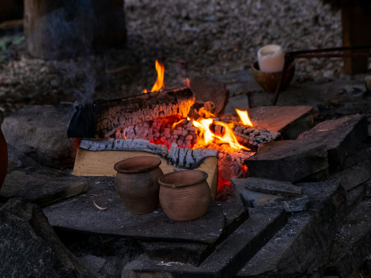 Clay pots warming beside an open fire on a stone hearth.