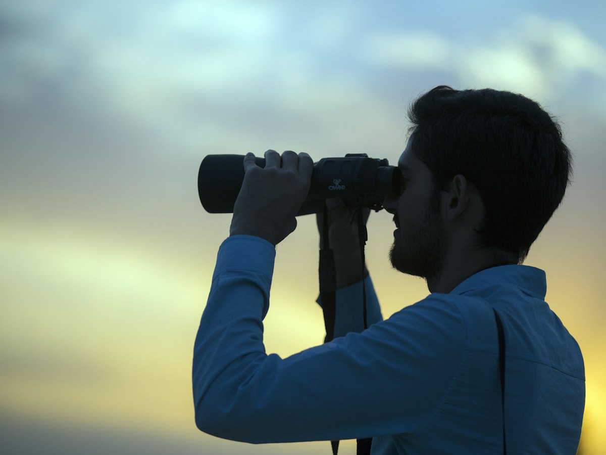 A man looking through binoculars at dusk.