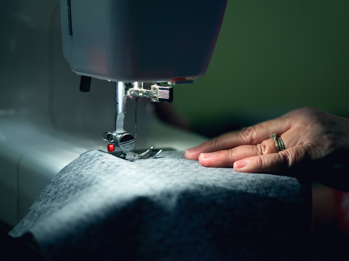Hands guiding fabric under a sewing machine needle.