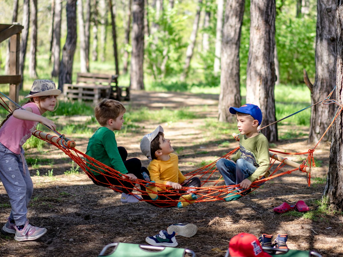 Small children playing with a hammock among the trees.