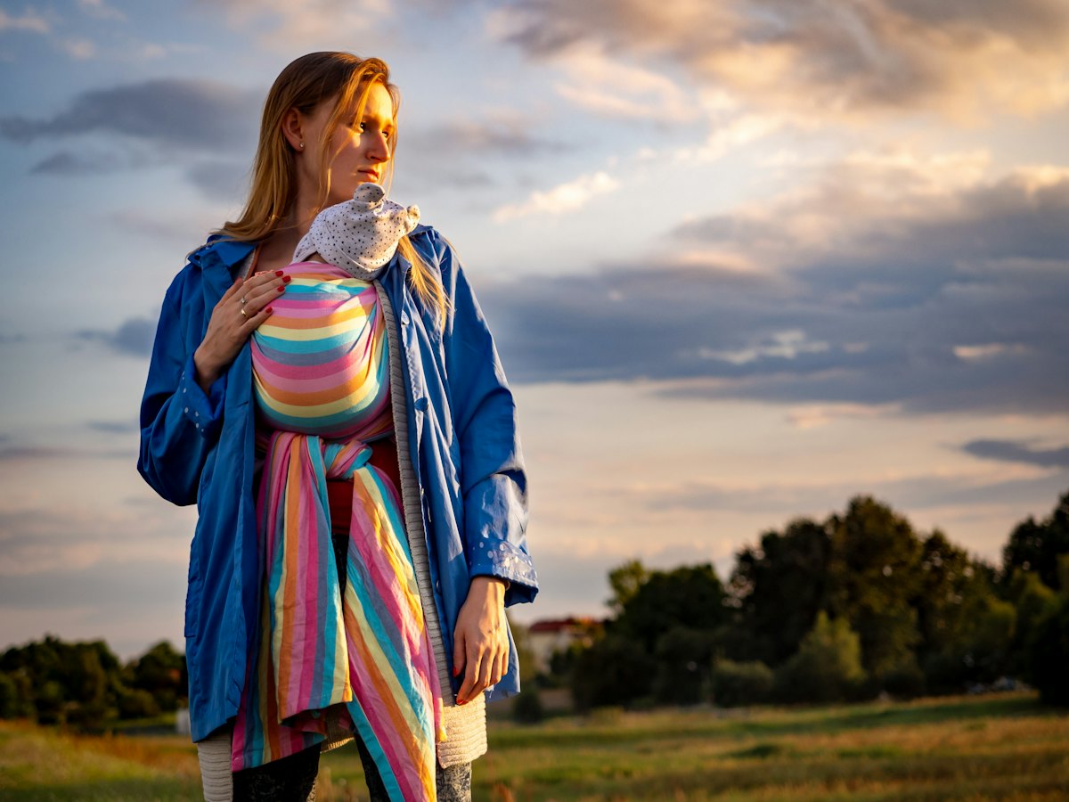 A mother carrying her baby in a wrap at sunset.