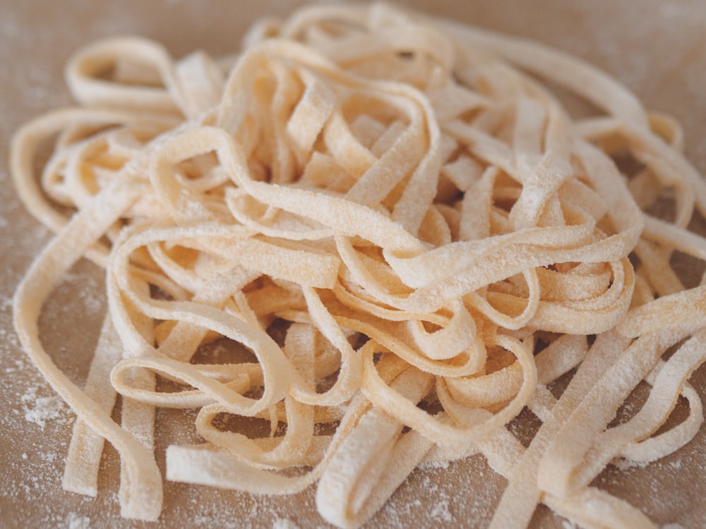 Hands rolling fresh pasta dough on a floured wooden board.