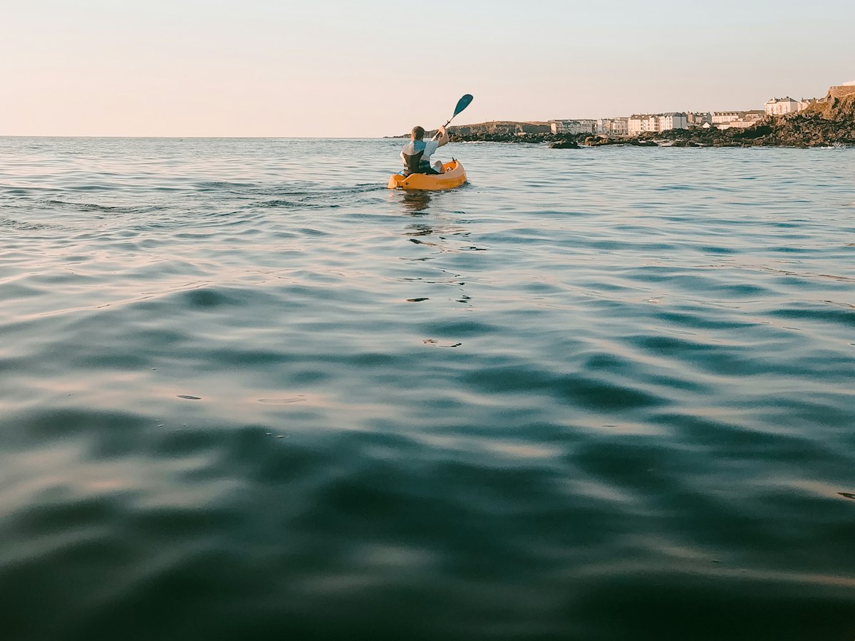 A kayaker paddling on calm sea water near the coast.