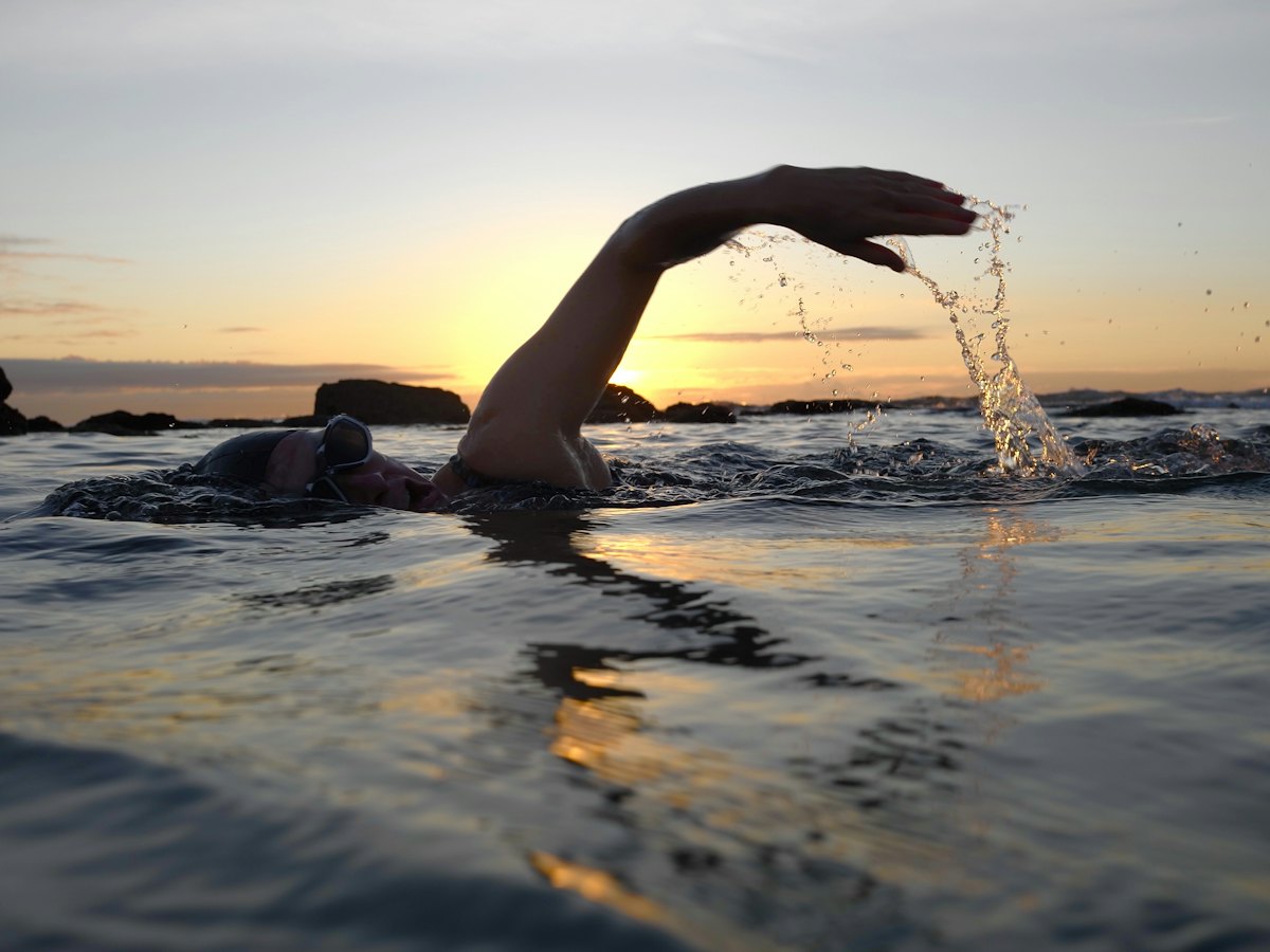 A swimmer mid-stroke in the sea at sunset.