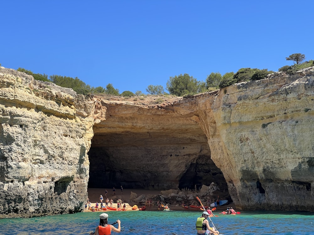 Kayakers paddling into the mouth of a sea cave beneath coastal cliffs.