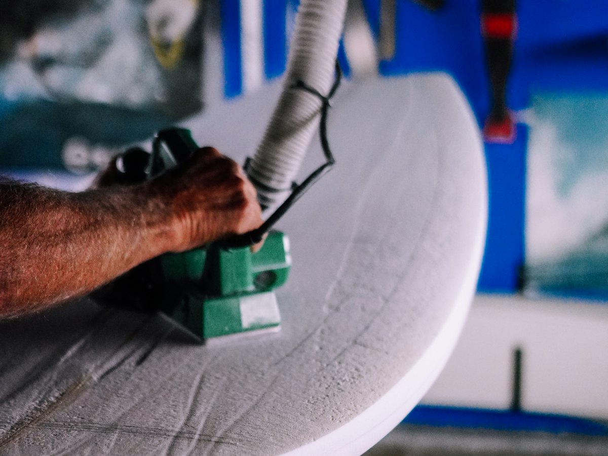 Hands sanding the rail of a surfboard.