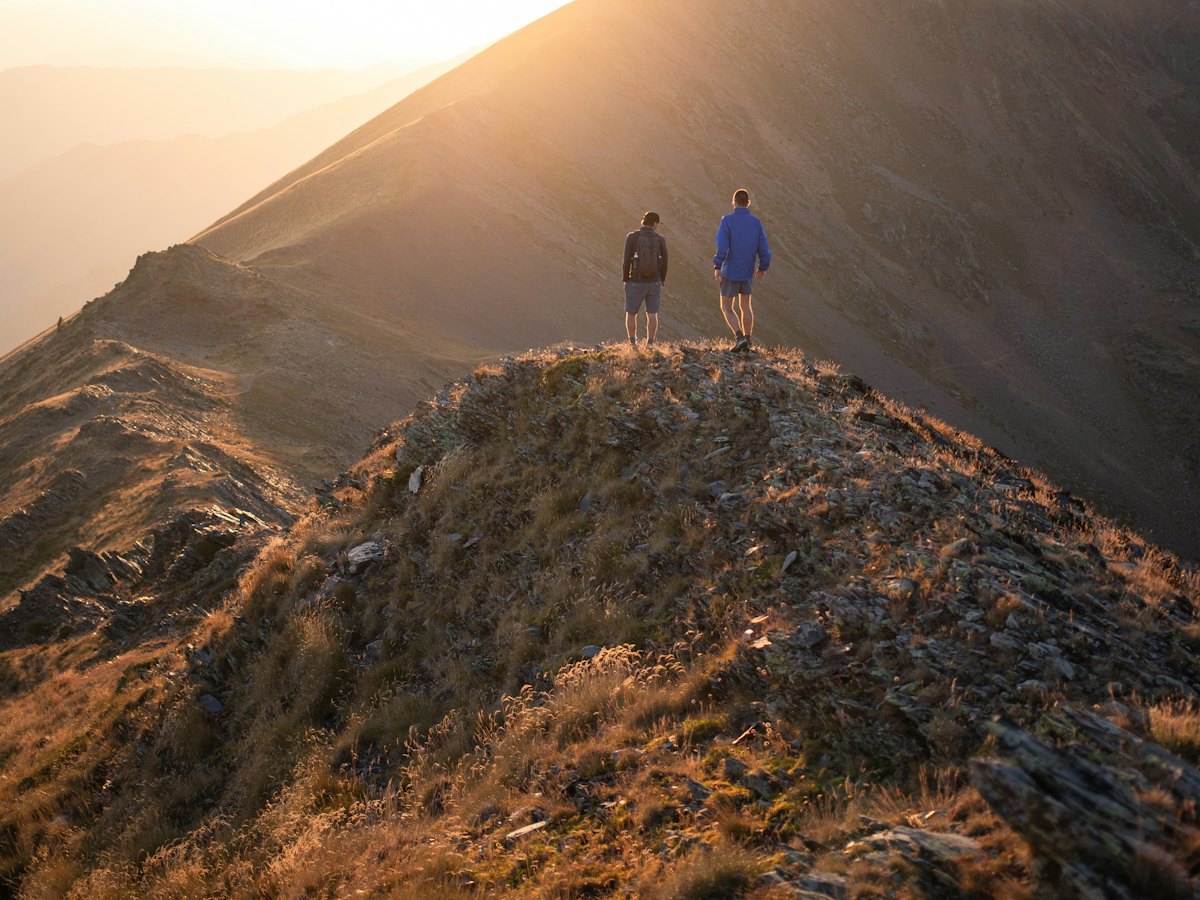 Two hikers on a mountain ridge at sunset.