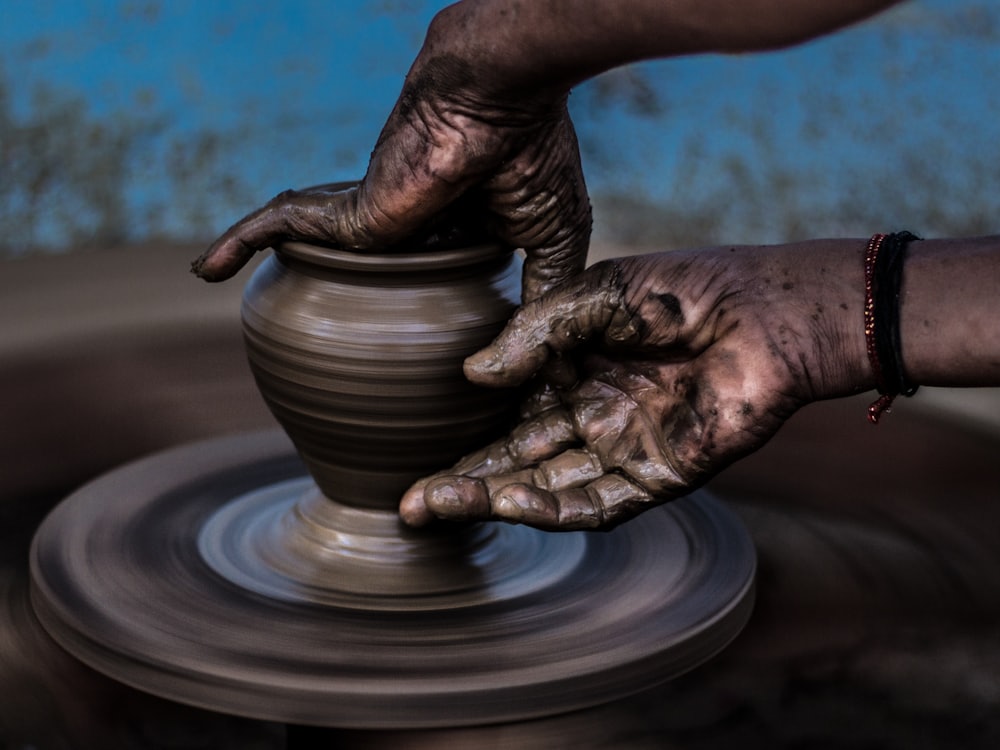 Hands centring wet clay on a moving pottery wheel.