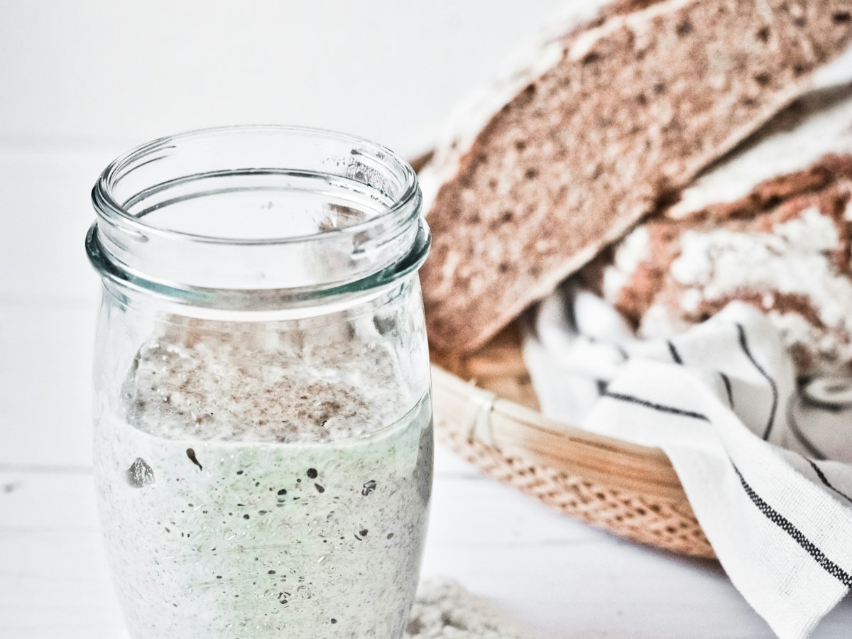A jar of bubbling sourdough starter beside a loaf.