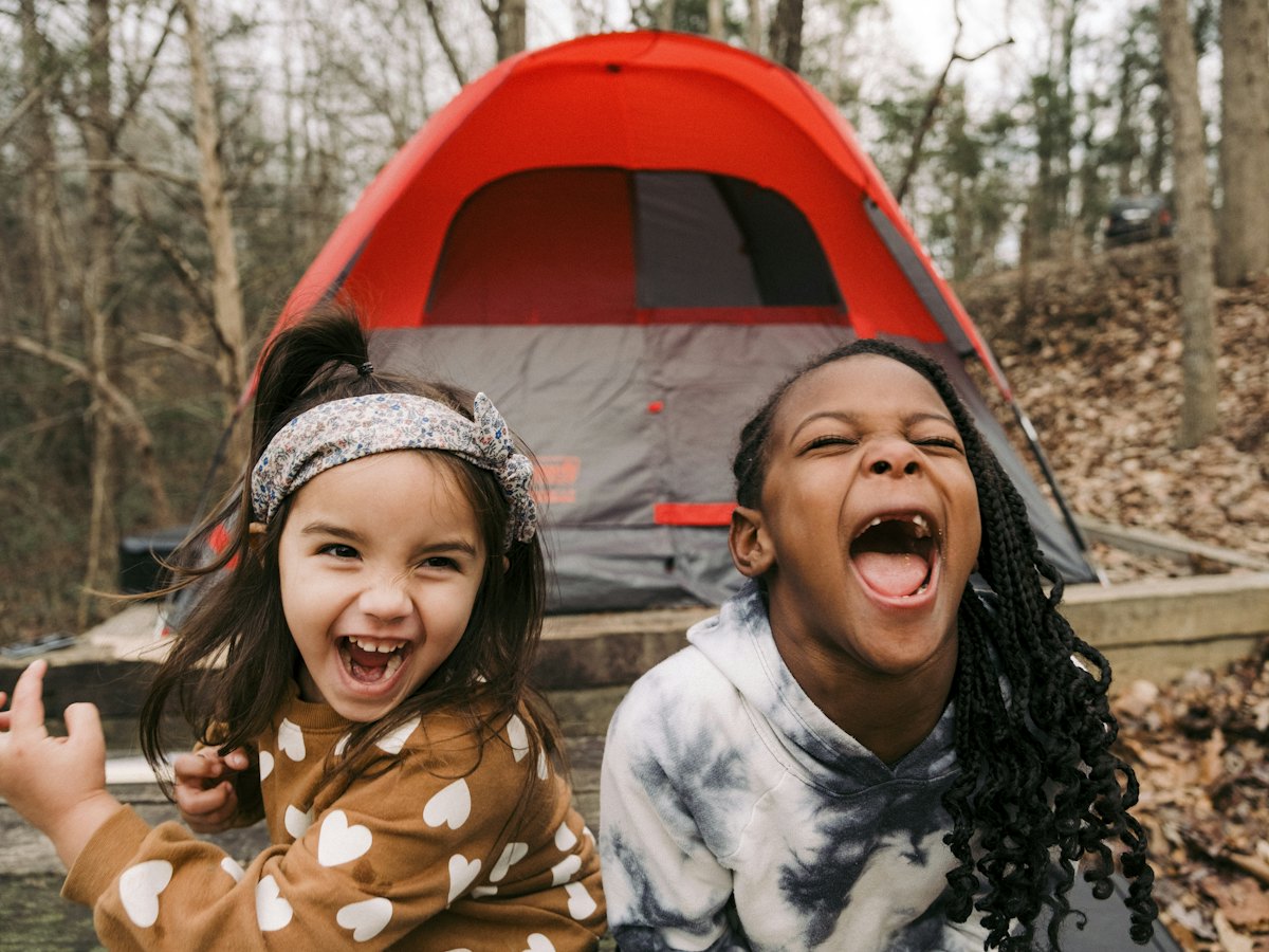 Two laughing children in front of a tent.